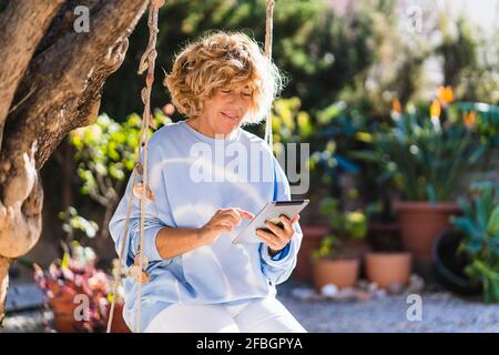 Mature woman using digital tablet while sitting on swing at back yard Stock Photo