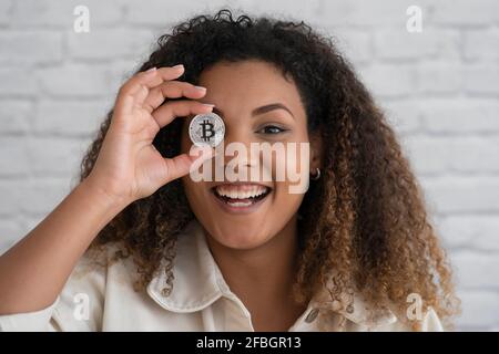 Smiling woman covering eye with silver cryptocurrency Stock Photo