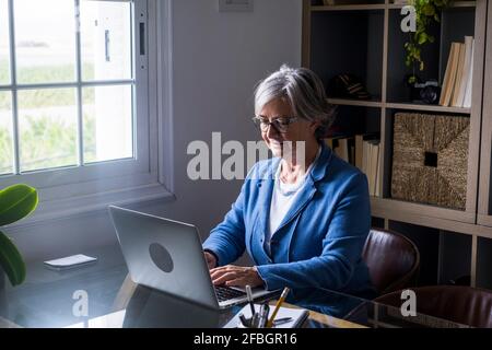 Smiling elderly female entrepreneur working on laptop while sitting at home Stock Photo