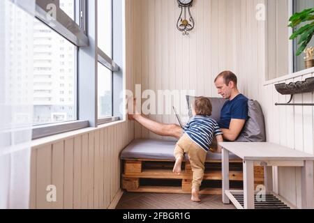 Boy looking at father using laptop on seat in home office Stock Photo