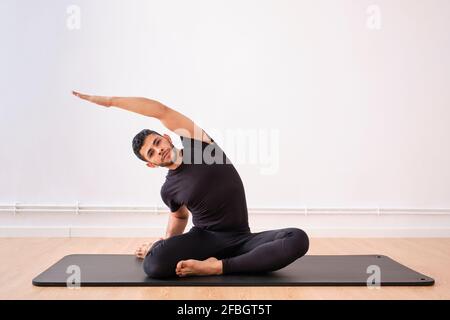 Handsome man doing stretching exercise on mat in exercise room Stock Photo