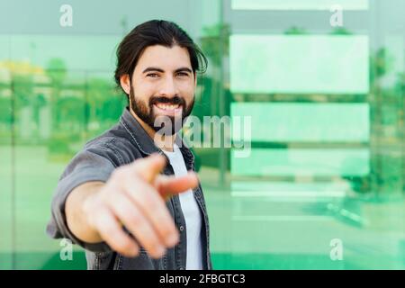 Smiling young man gesturing while standing in front of glass wall Stock Photo