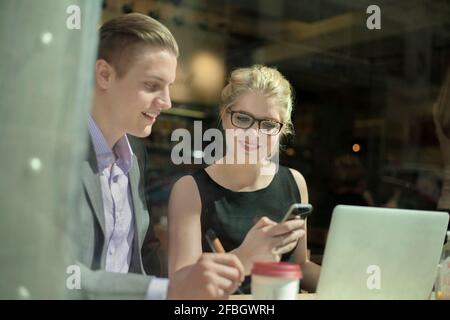 Smiling female entrepreneur texting through mobile phone while sitting by businessman Stock Photo