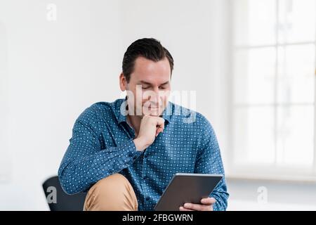 Businessman with hand on chin using digital tablet at workplace Stock Photo