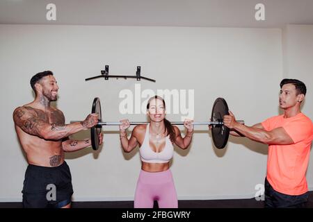 Sportswoman exercising with barbell by friends in gym Stock Photo