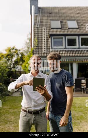 Father using digital tablet while standing by son in backyard Stock Photo