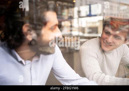 Male coworkers discussing in coworking office during coffee break seen through glass Stock Photo