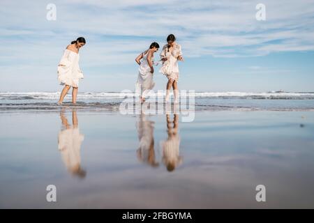 Female friends having fun while walking in water at beach Stock Photo