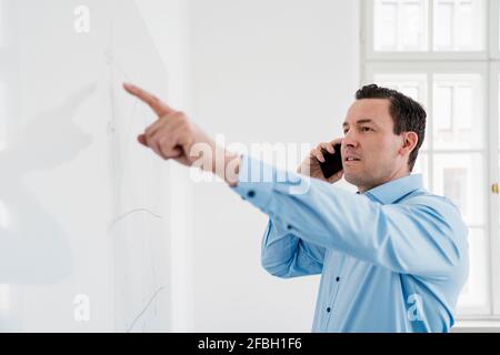 Male entrepreneur talking on phone while analyzing chart at office Stock Photo