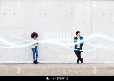 Businesswoman using mobile phone while standing by man with glowing wave pattern on footpath Stock Photo
