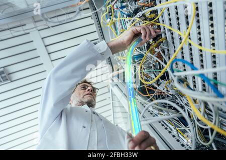 Mature male IT support plugging in fiber optic cable at data center Stock Photo