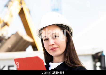 Female engineer in hardhat holding clipboard at site Stock Photo