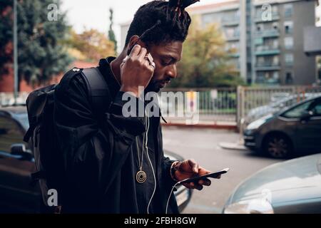Man adjusting in-ear headphones while using mobile phone Stock Photo
