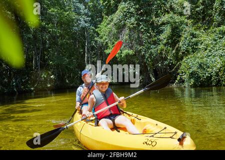 Cheerful daughter kayaking with oar while sitting against father in canoe Stock Photo