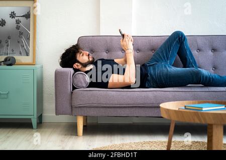 Relaxed young man using smart phone while lying on sofa at home Stock Photo