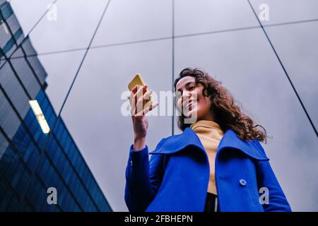 Smiling female freelance worker using mobile phone in front of building Stock Photo