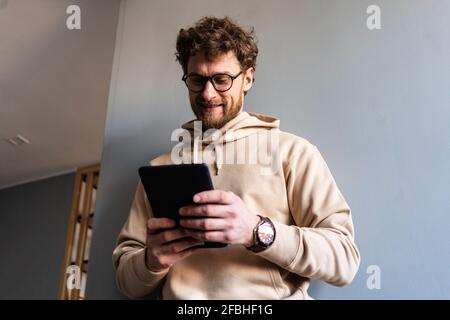Smiling man wearing eyeglasses using digital tablet at home Stock Photo