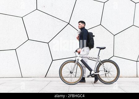 Young man wheeling bicycle by textured white wall Stock Photo