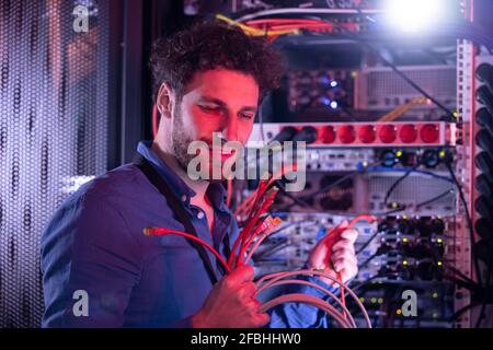 Male IT technician looking at patch cord cables while standing by server rack Stock Photo