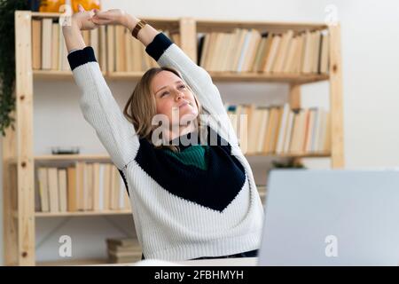 Woman stretching hands while sitting by laptop at home Stock Photo