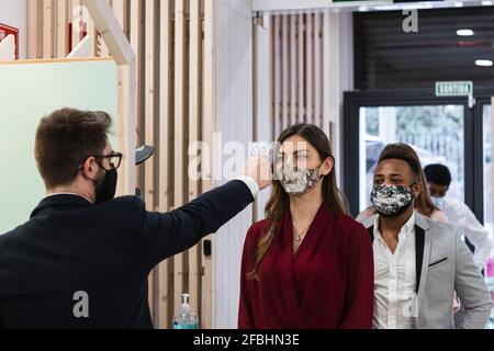 Man checking temperature of employees with face mask through infrared thermometer at office Stock Photo