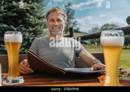 Smiling bearded man holding menu while sitting in beer garden Stock Photo