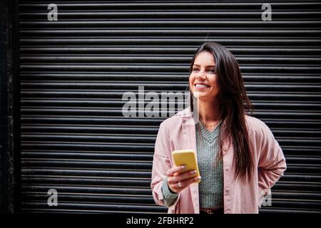 Smiling woman looking away while standing in front of closed shutter Stock Photo