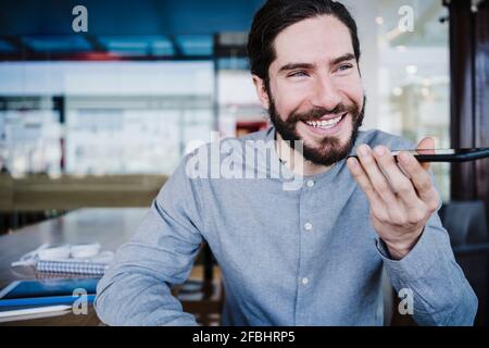 Smiling businessman talking on speaker through smart phone at work place Stock Photo