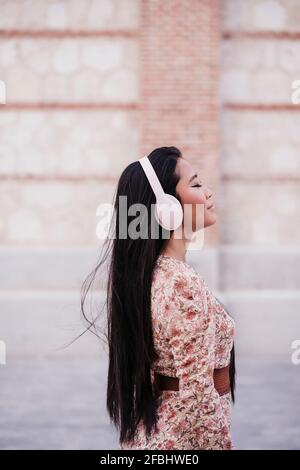 Woman with long hair wearing headphones while standing near wall Stock Photo