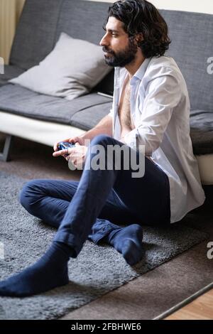 Young man playing video game while sitting in front of sofa at home Stock Photo