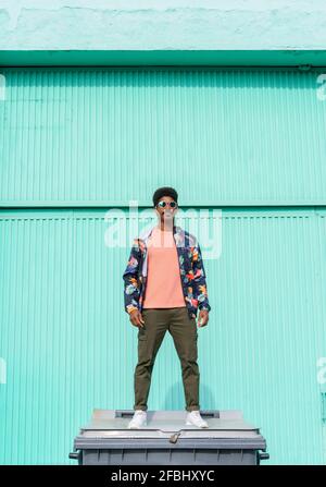 Handsome man standing on garbage bin in front of turquoise wall Stock Photo