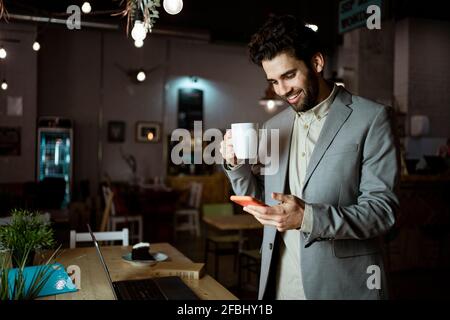 Smiling male entrepreneur using smart phone while having coffee in coffee shop Stock Photo