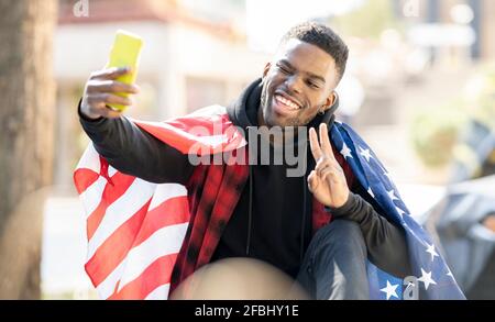Young man taking selfie with American flag while showing peace sign and winking Stock Photo