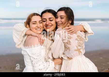 Happy young woman embracing friends at beach Stock Photo