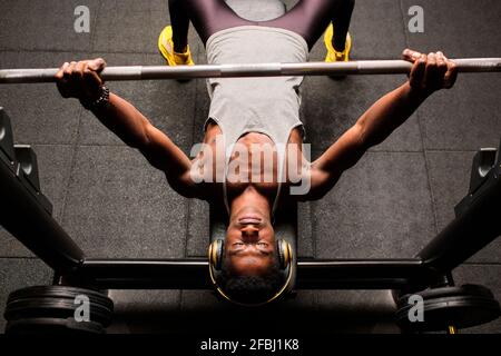 Determined young man doing bench press while listening music through headphones in gym Stock Photo