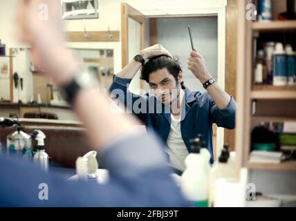 Portrait of barber fixing hair in front of mirror in barber shop Stock Photo