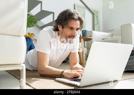 Man using laptop while lying on floor at home Stock Photo