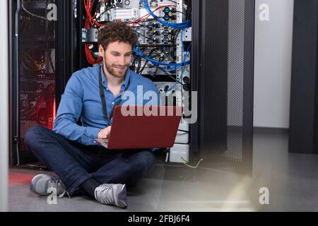 Male IT engineer working on laptop in front of rack in data center Stock Photo