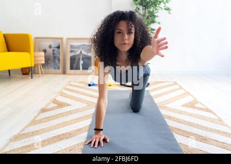 Curly haired woman stretching hand while exercising in living room