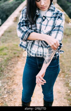 Mid adult woman with tattoo rolling up sleeves Stock Photo