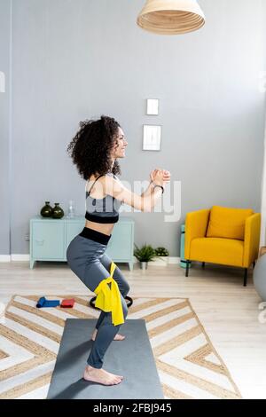 Smiling woman looking away while exercising with resistance band in living room Stock Photo