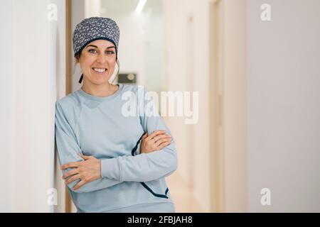 Smiling dentist wearing surgical cap standing with arms crossed at clinic corridor Stock Photo