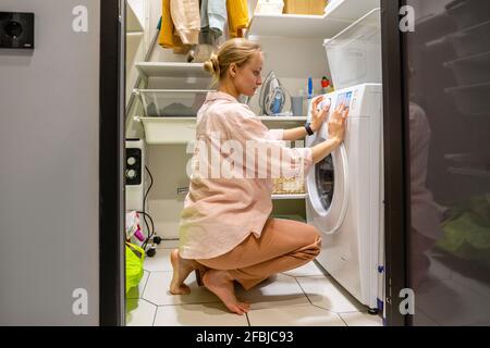 Young woman operating washing machine at home Stock Photo