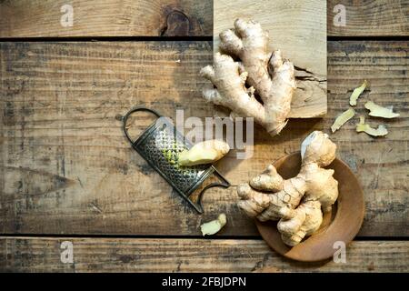 Ginger roots and old grater lying on wooden surface Stock Photo