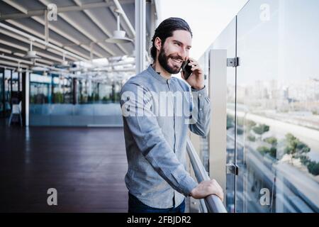 Creative businessman talking on mobile phone while looking though glass in office Stock Photo