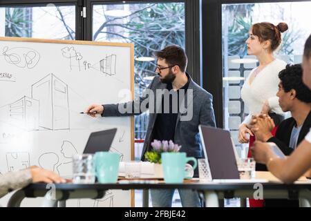 Young entrepreneur giving presentation to colleagues in meeting Stock Photo