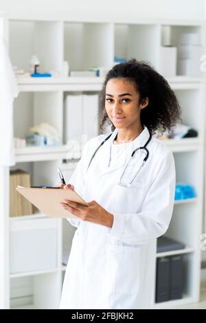Smiling young doctor holding clipboard and pen while standing in clinic Stock Photo