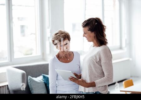 Surprised senior woman looking at digital tablet held by granddaughter at home Stock Photo
