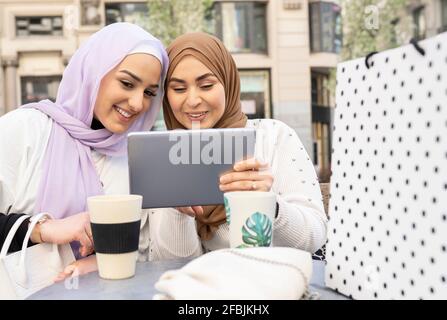 Smiling Arab women using digital tablet at sidewalk cafe in city Stock Photo