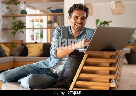 Happy male freelancer using laptop while sitting at home Stock Photo